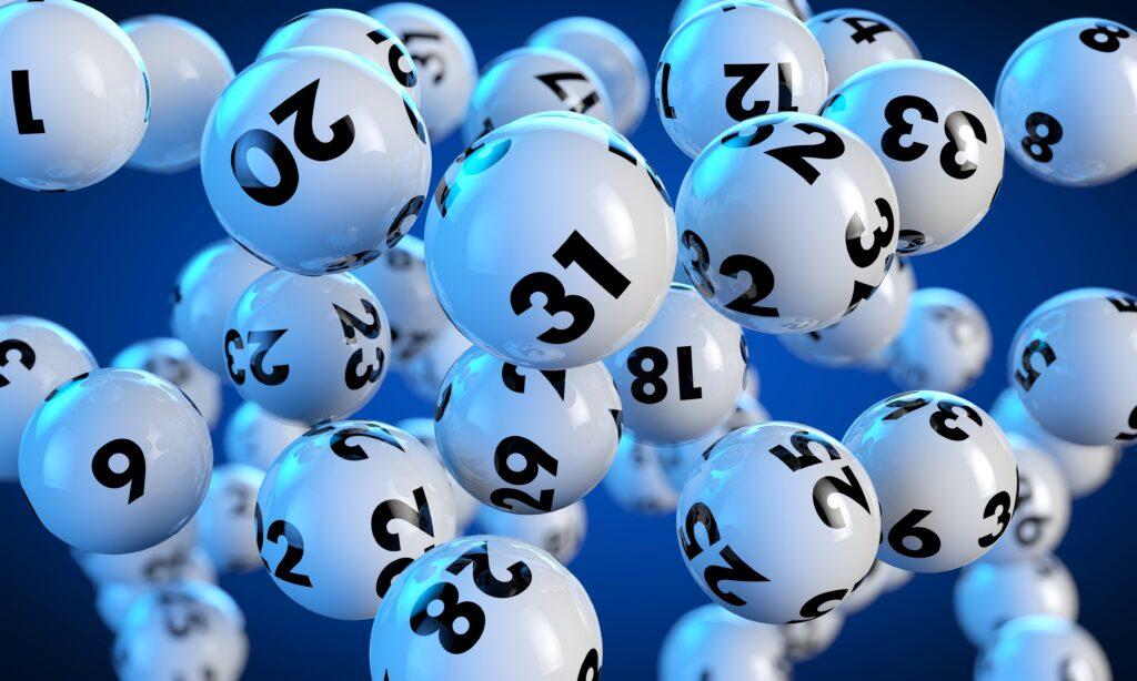 Weiße Lottozahlen-Bälle mit schwarzen Zahlen schweben vor einem blauen Hintergrund.