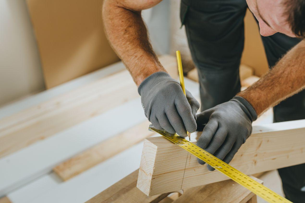 Handwerker markiert ein Massivholz-Bauteil praezise mit Massband und Bleistift bei einem moebelbau berlin Auftrag