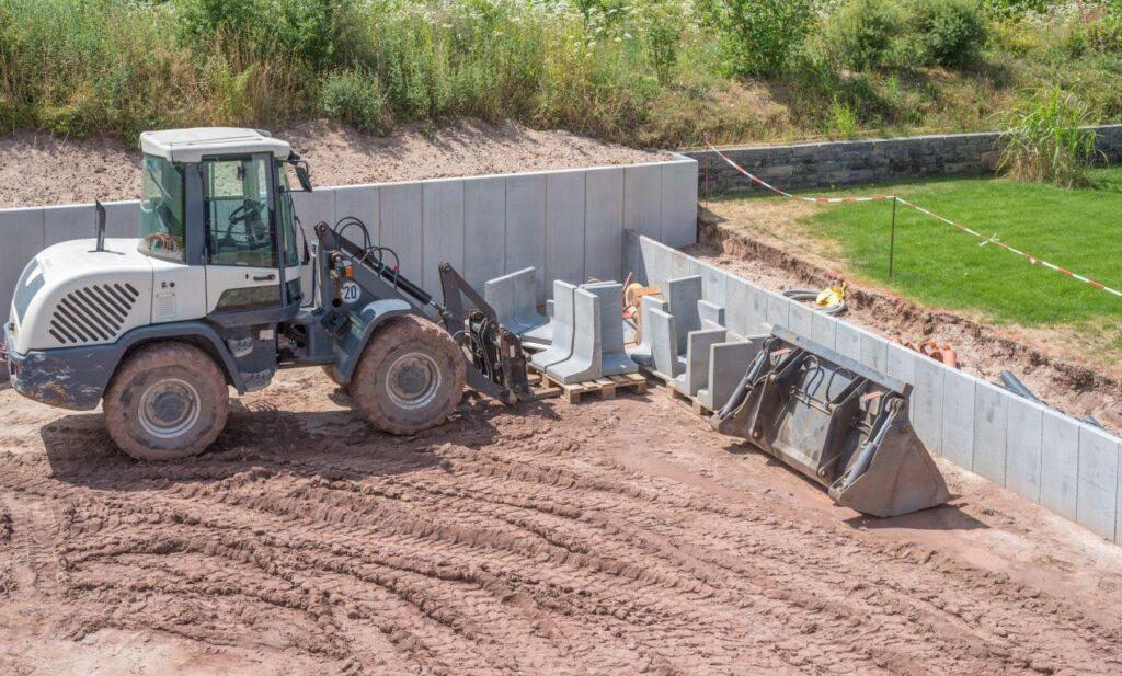Radlader mit verschiedenen Anbaugeraeten wie Tiefloeffel auf Baustelle – Erdarbeiten vor Fundamentlegung im Gange